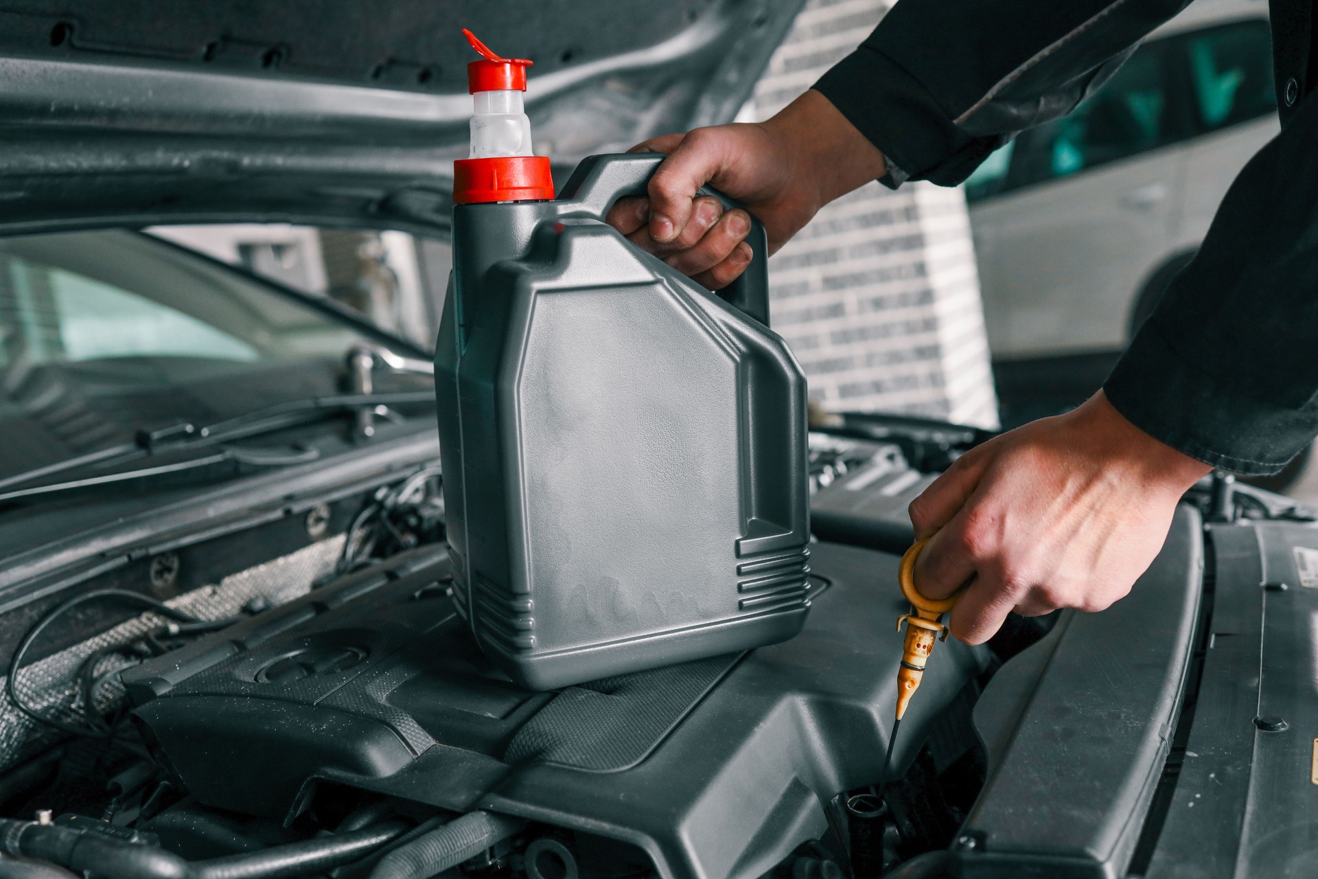 Close-up of a mechanic holding a bottle of motor oil and an oil dipstick, performing an oil change in a vehicle. Highlights car maintenance and servicing tasks